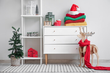 Chest of drawers with winter clothes and Christmas decorations near white wall