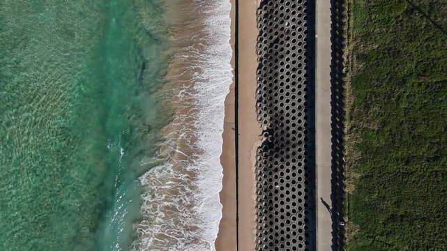 Top down of Cronulla boardwalk and breakwater with crashing waves running parallel to beach and sea with visible wave lines, Sydney NSW Australia