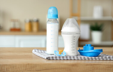 Bottles of baby milk formula, pacifier and toy boat on wooden kitchen counter