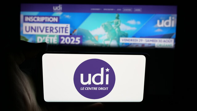 Stuttgart, Germany - 06-26-2025: Person holding cellphone with logo of Union des Democrates et Independants (UDI) on screen in front of webpage. Focus on phone display.