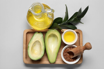 Wooden board with fresh avocado, flax seeds and decanter with oil on grey background