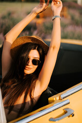 Young woman enjoying the sun in a classic convertible car surrounded by nature