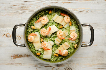 Delicious shrimp and fish rice dish prepared in a gray pot with green herbs on a wooden table