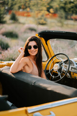 Young woman smiling in a vintage yellow convertible car on a sunny day