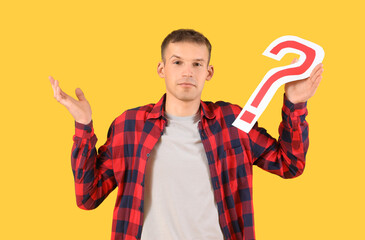 Young man with paper question mark shrugging on yellow background
