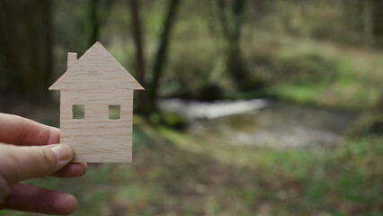 A man's hand holds a wooden model of a house.