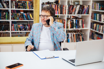 Business man talking on phone working on laptop online in library