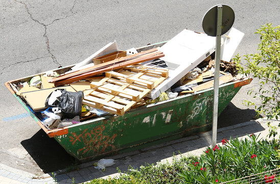 Contenedor met&aacute;lico de hierro verde de obra, basura, pal&eacute;s de madera y restos de material de demolici&oacute;n, reforma y construcci&oacute;n en la calle