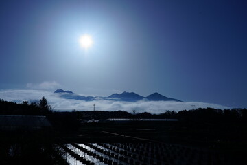 早朝の陽光の下に横たわる山並みの足元に雲が佇む
