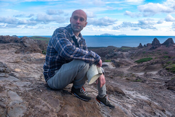 young traveler man sits on volcanic rocks, enjoying breathtaking landscape volcanic Madeira Island during journey, Viewpoint Calhau da Furna do Bode, discovery archipelago travel, adventure vacation