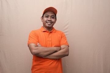 Smiling Southeast Asian man in orange uniform and cap standing confidently with arms crossed...