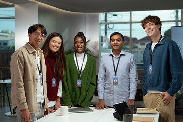 Diverse business team meeting in modern office smiling and standing together around table with laptop and documents showing collaboration and positive work environment