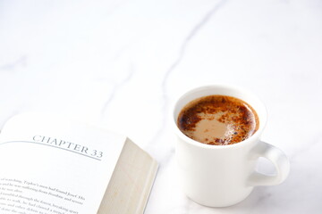 ページを開いたペーパーバック（洋書）とコーヒーの入ったコーヒーカップで、コーヒーを飲みながら読書を楽しんでいるイメージ
