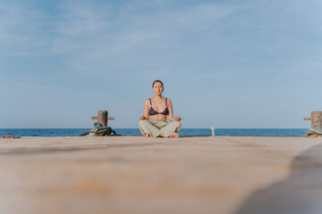 Young woman meditating on pier at sunrise, embracing serenity and mindfulness by the sea