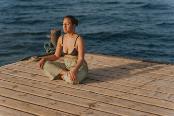 Young woman meditating on a wooden pier at sunset, embracing serenity by the sea