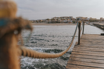 Rope connecting wooden posts on pier over water with resort in background