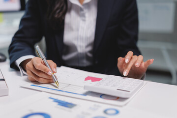 Businesswoman analyzing financial charts and using calculator in office