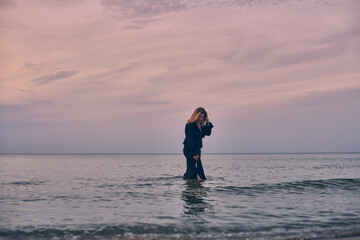 Young woman walks alone in tranquil sea under pastel sky. Her contemplative stance against soothing ocean backdrop evokes introspection and peace
