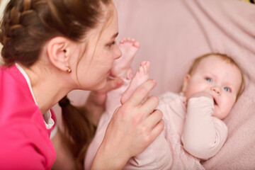 Young mother with brown hair engages tenderly with baby girl. Mothers affectionate gesture captured...