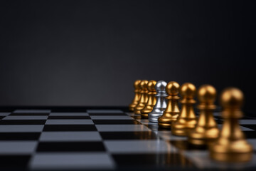 A silver pawn stands in the middle of a row of golden pawns,