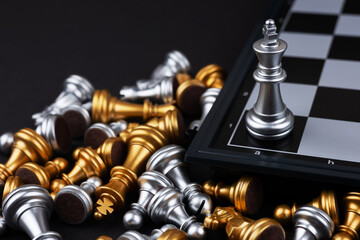 top view shot of silver king surrounded with silver and golden chess pieces a lying behind chess board