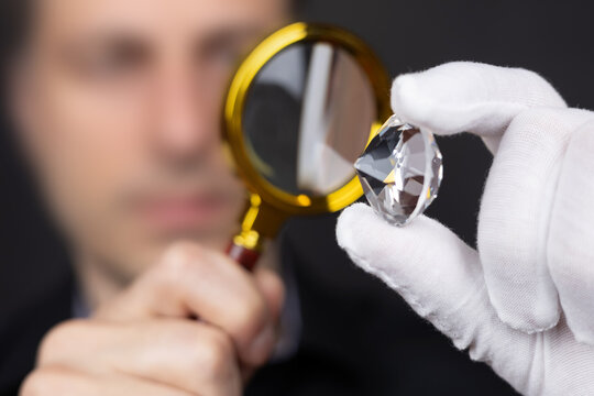 Man jeweller examines polished diamond through magnifier. Buyer checking diamond.