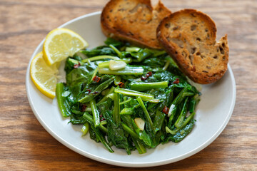 Sauteed Chicory Greens - a traditional Italian side dish on a plate served with toasted bread and slices of lemon.