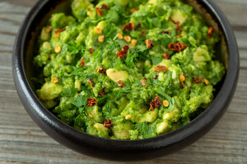 Homemade guacamole sprinkled with hot chili flakes in a bowl on a rustic wooden table. 