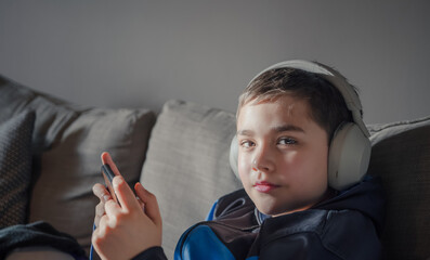 Primary school Kid using mobile phone searching information on internet for homework,Child wearing...