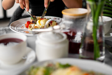 Close-up of person eating melted cheese dish with tomatoes and greens, served with tea on a rustic...