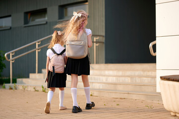 Obraz premium schoolgirls with backpacks walking to school building in uniform. young students heading to class represent education, learning, and friendship, capturing back-to-school season vibe.