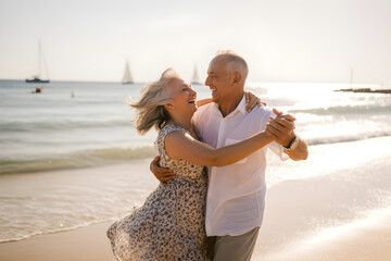 Happy senior couple dancing on the beach at sunset