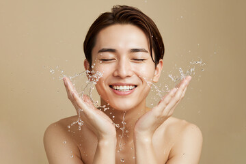 Asian man washing face with water splash on beige background, copy space