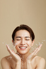 Asian man washing face with water splash on beige background, copy space