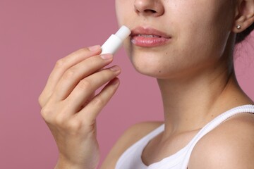 Young woman with lip balm on pink background, closeup