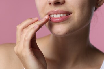 Young woman with lip balm on her lips against pink background, closeup