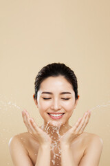 Asian woman washing face with water splash on beige background, copy space