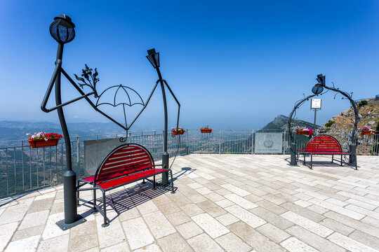 View of red benches and decorative iron figures stand out against the bright blue sky and panoramic landscape, Cilento, Trentinara, Campania, Italy.