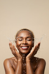 Portrait of senior African woman washing face with water splash on beige background, copy space