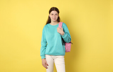 Teenage girl with backpack on yellow background