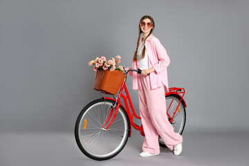 Smiling woman in sunglasses and bicycle with basket of flowers against grey background