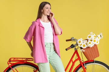 Smiling woman and bicycle with basket of flowers against light green background