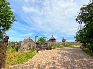 A pleasant walk along the ancient wooden fence and watchtowers of the Zaporizhzhia Sich on Khortytsia Island under a blue, partly cloudy sky.