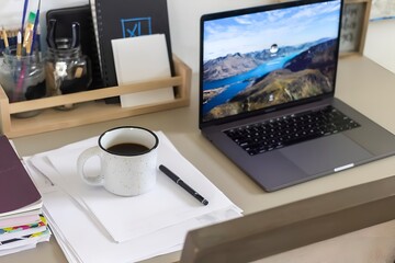 Modern home office workspace with laptop, coffee mug, hyper realistic papers, and stationery, cozy and productive remote work setup, bright and minimal desk environment, creative studio."