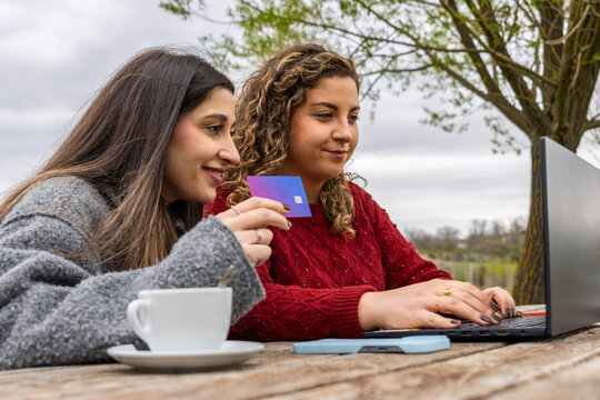 Two young women shopping online using laptop and credit card outdoors