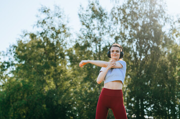 A woman stretches in a park, headphones on, enveloped in the tranquil beauty of nature and morning light.