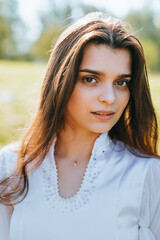 A woman in a shimmering white dress poses gracefully amidst sunlight, her expression serene and captivating.