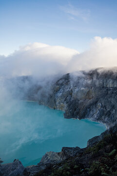 View of the striking turquoise crater lake steaming amidst rugged cliffs and swirling clouds, a volcanic spectacle, Ijen Volcano Crater, East Java, Indonesia.