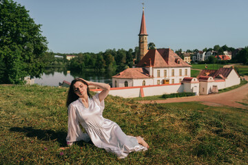A woman in a serene landscape, lounging thoughtfully on the grass, framed by historic architecture and clear skies.