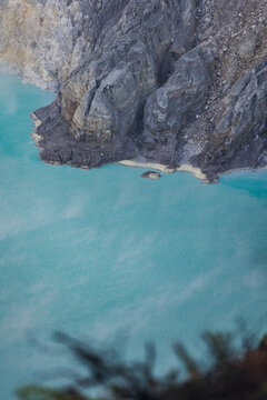 View of turquoise waters meet the rugged, dark volcanic rock in a mesmerizing dance of color and texture, Ijen Volcano Crater, East Java, Indonesia.
